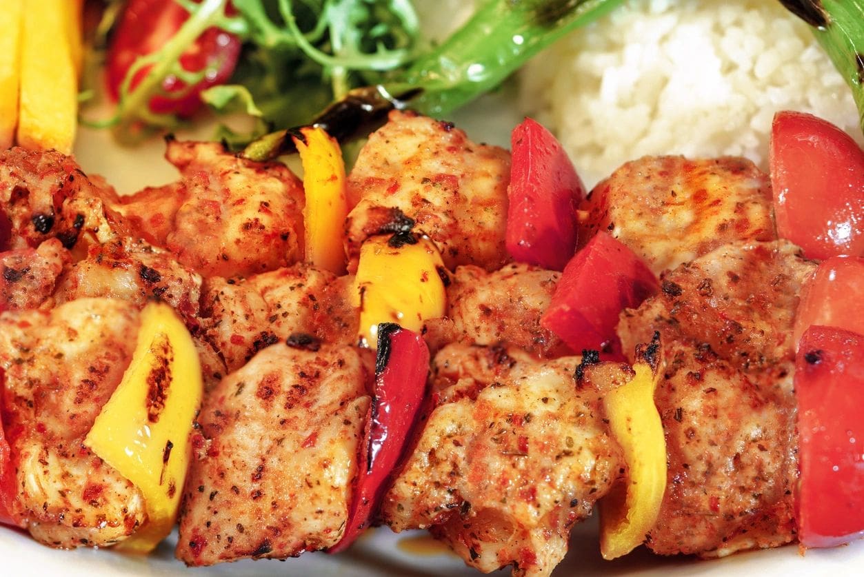 Chicken skewers, french fries and rice with leaf vegetable.